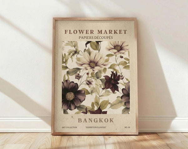 May include: Framed botanical poster with vintage-style illustration of purple and cream flowers with green leaves on aged paper background. Text reads "Flower Market Bangkok" at top and bottom. Natural wood frame sits on light wooden floor against white wall with soft shadows from window light.
