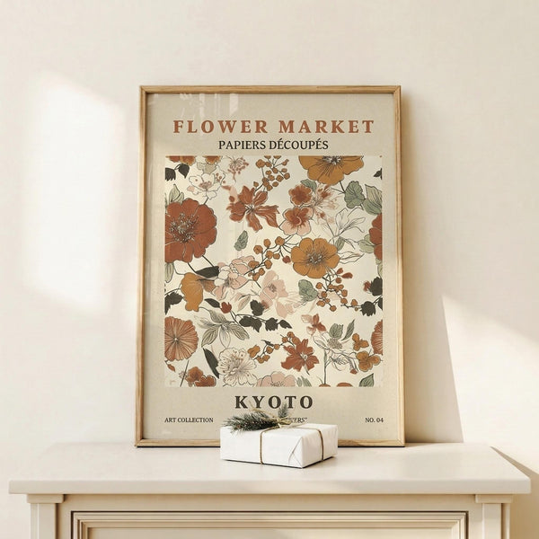 May include: Framed botanical poster with vintage-style floral illustration in warm earth tones including rust, amber, and sage green flowers and leaves on cream background, displayed on light wood console table with small white wrapped gift box beside it against neutral wall
