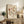 May include: Framed botanical poster with vintage-style floral illustrations in warm earth tones including rust, orange, and sage green flowers and leaves on cream background. Print displays on rustic wooden sideboard alongside fern plant, books, ceramic vase, and table lamp in cozy neutral-toned living room setting with leather furniture.