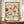 May include: Framed vintage-style botanical poster displaying various flowers in warm earth tones including rust, sage green, and cream colors. The artwork features "FLOWER MARKET" and "PAPIERS DÉCOUPÉS" at top, "KYOTO" prominently in center, with "ART COLLECTION" and "EXHIBITION FLOWERS" at bottom. Dark wooden frame sits on light wood sideboard next to white ceramic vase and stack of books against cream wall with white trim molding.