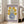 May include: Framed vintage-style poster showing six yellow flowers with brown centers in a blue polka-dotted vase, with "Flower Market" text at top and "Galerie d'Art Moderne" at bottom on purple border. Light wood frame leans against white wall next to beige couch in bright, minimalist living room with large windows and natural light.