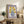 May include: A framed vintage-style floral poster with purple border displaying yellow flowers in a blue polka-dotted vase, positioned on a rustic wood sideboard alongside a fern plant, ceramic vases, and books in a cozy living room setting with neutral tones and natural lighting.