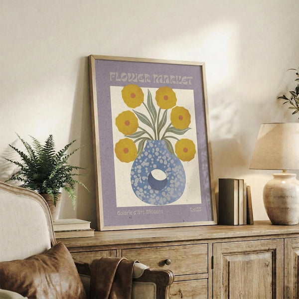 May include: A framed vintage-style floral poster with purple border displaying yellow flowers in a blue polka-dotted vase, positioned on a rustic wood sideboard alongside a fern plant, ceramic vases, and books in a cozy living room setting with neutral tones and natural lighting.
