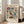 May include: Vintage-style botanical poster in light wood frame leaning against white wall next to beige armchair. Features colorful folk art flowers in teal, orange, burgundy on cream background with "FLOWER MARKET," "PAPIERS DÉCOUPÉS," and "MEXICO" text. Sunlight streams through windows onto hardwood floor.