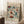 May include: Framed vintage-style floral poster with decorative flowers in teal, orange, rust, and cream colors, leaning against white paneled wall. Coffee cup on wooden block nearby, cozy textured blanket visible. Poster features ornate botanical design with "FLOWER MARKET" and "MEXICO" text in burgundy and teal lettering.