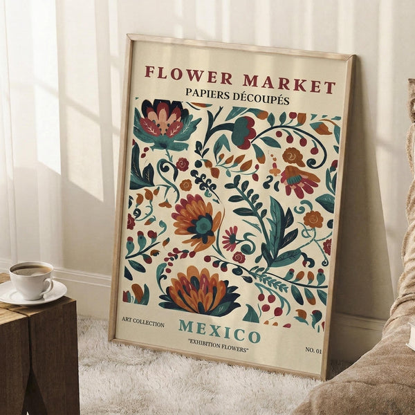 May include: Framed vintage-style floral poster with decorative flowers in teal, orange, rust, and cream colors, leaning against white paneled wall. Coffee cup on wooden block nearby, cozy textured blanket visible. Poster features ornate botanical design with "FLOWER MARKET" and "MEXICO" text in burgundy and teal lettering.