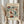 May include: hands holding a framed vintage-style botanical poster featuring colorful folk art flowers in burgundy, teal, and orange tones against cream background. Person wears beige ruffled sleeves, holds dried wheat stems, standing by white curtained window in soft natural lighting.