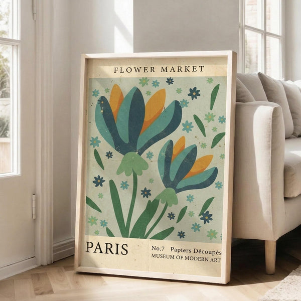May include: Framed botanical poster with stylized green and orange flowers on cream background, displayed against white wall next to beige upholstered sofa in bright living room with large windows and natural light streaming across hardwood floors.