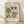 May include: Framed botanical poster print with vintage-style floral pattern in earthy greens, rust orange, and cream colors, displayed against white textured wall on light wood flooring. Features decorative flowers, leaves, and vines in folk art style with "FLOWER MARKET" and "SANTORINI" text headers. Natural wood frame catches soft window light creating gentle shadows.