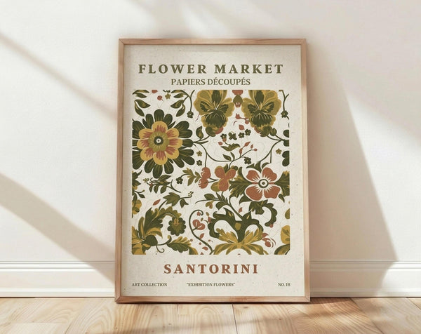 May include: Framed botanical poster print with vintage-style floral pattern in earthy greens, rust orange, and cream colors, displayed against white textured wall on light wood flooring. Features decorative flowers, leaves, and vines in folk art style with "FLOWER MARKET" and "SANTORINI" text headers. Natural wood frame catches soft window light creating gentle shadows.