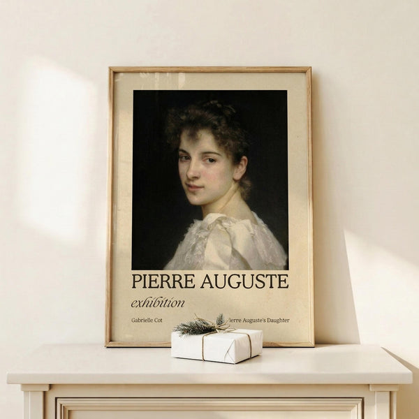 May include: Framed art print featuring a classical portrait of a young woman with dark curly hair wearing a white dress against a black background. The poster displays "PIERRE AUGUSTE exhibition" text below the portrait. Shows cream matting in natural wood frame, positioned on white wooden surface with small wrapped gift box nearby. Soft lighting creates gentle shadows on neutral wall background.