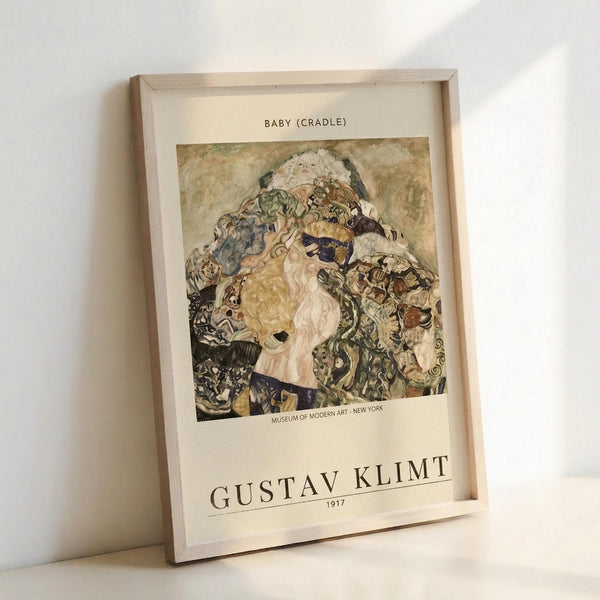 May include: Framed art print leaning against white wall showing Gustav Klimt's Baby (Cradle) painting from 1917. The artwork depicts swirling, organic forms in earth tones with intricate patterns characteristic of Klimt's style. Museum of Modern Art New York attribution visible below the image. Light wood frame with white matting, casting soft shadows on the wall.