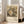 May include: Framed art print leaning against white wall next to beige sofa in bright room with windows. Print shows Gustav Klimt's colorful painting of a baby surrounded by ornate patterned fabrics and decorative elements in earth tones, blues, and golds. Cream-colored poster with black text identifying the artwork, artist name, and museum attribution. Light wood frame, approximately 2-3 feet tall, positioned on light wooden floor.