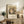 May include: Framed Gustav Klimt museum exhibition poster displaying Baby (Cradle) artwork in warm earth tones and intricate patterns, positioned on rustic wooden sideboard alongside fern plant, ceramic vase, and leather chair in cozy neutral-toned living room setting with soft natural lighting