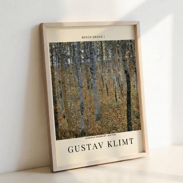 May include: Framed art print of Gustav Klimt's "Beech Grove I" showing tall birch trees with white bark in an autumn forest with golden-yellow foliage covering the ground. The poster has cream-colored borders with black text identifying the artwork and Museum of Modern Art New York. Natural wood frame leans against white wall casting soft shadows.