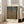 May include: Framed art print of Gustav Klimt's Beech Grove I painting featuring golden autumn birch trees with white bark against yellow foliage, displayed in a light wooden frame leaning against white walls near a beige upholstered chair in a bright room with tall windows and natural lighting on light wood floors.