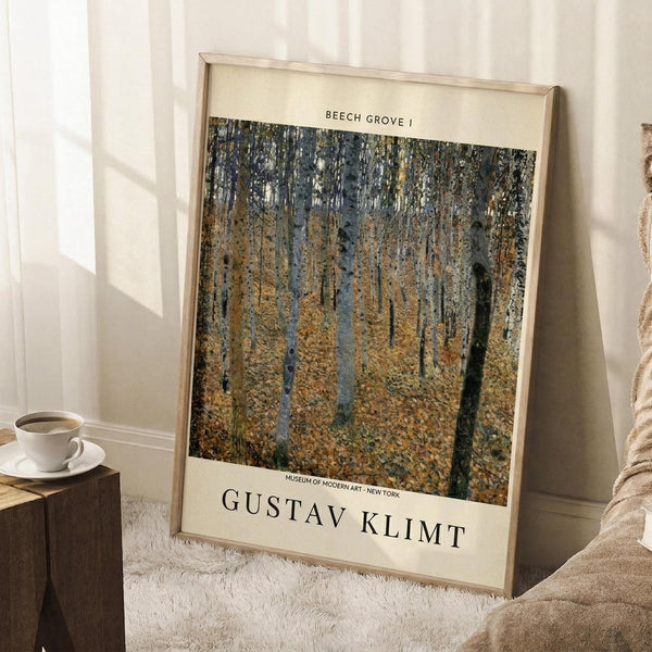 May include: Framed museum poster print featuring Gustav Klimt's "Beech Grove I" artwork showing tall trees with golden autumn foliage in an impressionistic style. The poster has cream colored borders with black text identifying the artwork and Museum of Modern Art. Shown leaning against white paneled wall next to beige armchair and wooden side table with white coffee cup and saucer, positioned on textured white area rug.