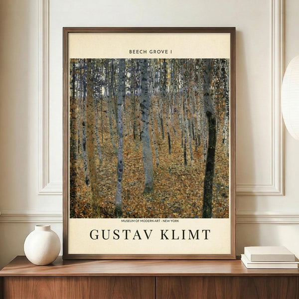 May include: Framed art print of Gustav Klimt's Beech Grove I displayed on a wooden sideboard against cream-colored walls with white molding. The poster features tall birch trees with white bark in an autumn forest with golden-yellow foliage covering the ground. Dark wood frame surrounds the cream-colored print with black text identifying the artwork and Museum of Modern Art. White ceramic vase and stacked books positioned nearby for scale.