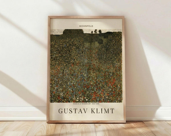 May include: Framed art print of Gustav Klimt's "Mohnfeld" showing a textured landscape with wildflower meadow in foreground filled with red poppies and small white flowers, rolling green hills and trees in background. Cream-colored poster with museum attribution text and artist name in serif font, displayed in light wood frame against white wall on wooden floor with natural window light casting shadows.