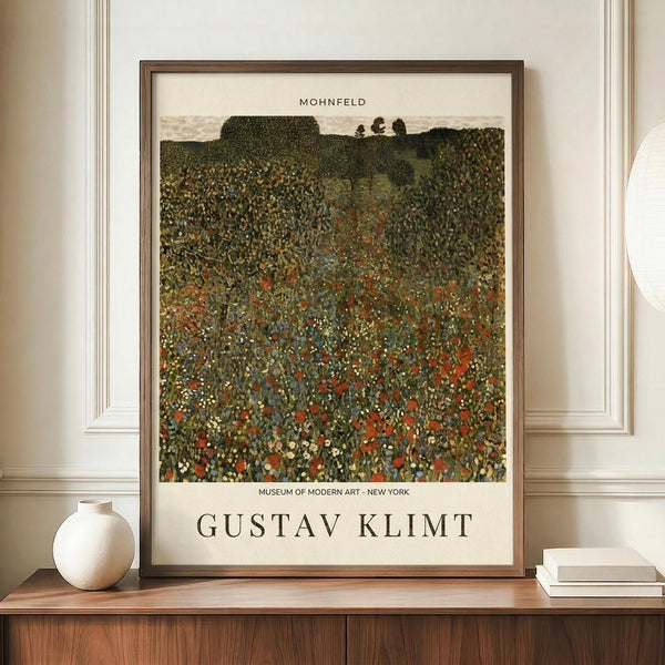 May include: Framed Gustav Klimt museum poster displaying a vibrant meadow landscape filled with colorful wildflowers in greens, reds, and blues, with rolling hills and trees in the background. The artwork shows Klimt's distinctive pointillist style with dense, decorative flower patterns. The poster features "MOHNFELD" at top and "GUSTAV KLIMT" and "MUSEUM OF MODERN ART - NEW YORK" at bottom in black text on cream background. Displayed on a wooden credenza alongside a white