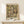 May include: Framed poster displaying Gustav Klimt's 1916 Portrait of Friederike Maria Beer, featuring a woman with long dark hair in an ornate patterned dress surrounded by colorful figures and decorative elements in Klimt's distinctive Art Nouveau style. The vintage-style print is in a light wood frame, positioned on a pale wooden shelf next to a small white gift box with evergreen sprig against a cream wall.