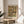 May include: Framed art print featuring Gustav Klimt's ornate portrait from 1916, displaying a central female figure surrounded by vibrant decorative patterns in yellows, greens, and earth tones. The wooden-framed poster sits on a round light wood side table next to a beige upholstered chair, with natural sunlight streaming across white walls and a plant visible in the corner of the modern minimalist room setting.
