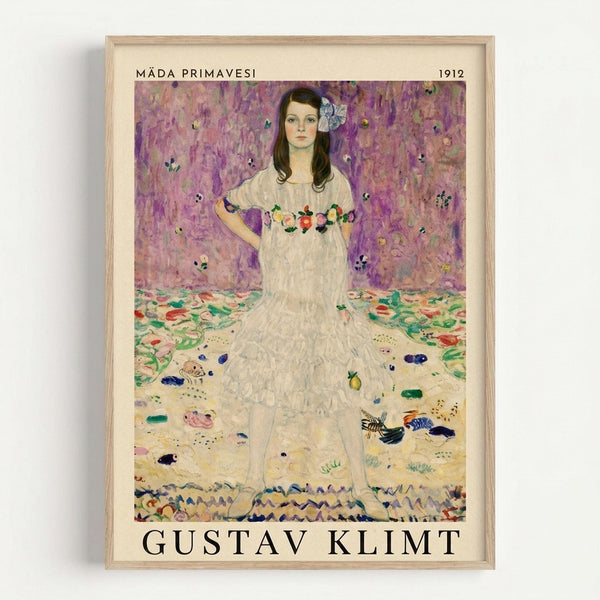 Framed art print featuring a young girl in a white ruffled dress with floral embroidery, standing against a purple floral wallpaper background. The painting shows decorative elements scattered on the floor around her feet. Text at top reads "MÄDA PRIMAVESI" and "1912", with "GUSTAV KLIMT" at bottom in black letters. Light wooden frame on white background.