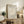 May include: Framed beige and cream botanical poster featuring white coral-like plant form, displayed on rustic wood sideboard in neutral living room with fern plant, ceramic vase, books, and beige upholstered chair with brown leather throw pillow