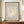 May include: Framed Matisse exhibition poster with cream coral silhouette on sage green background, displayed on wooden credenza beside white ceramic vase and stacked books in elegant room with beige walls and white molding