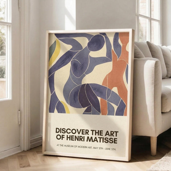May include: A framed art poster featuring abstract blue dancers in Henri Matisse's cut-out style, with flowing purple-blue figures, orange and yellow accents on cream background. The poster advertises a Museum of Modern Art exhibition from May 5th to June 5th. Displayed in a bright living room corner next to a beige armchair, natural light streaming through white-framed windows.
