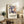 May include: Framed art print featuring abstract blue figures in Matisse's cut-out style with orange and yellow accents, displayed on rustic wood credenza alongside fern plant, ceramic vase, and books in warm-toned living room setting with cream upholstered chair