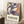 May include: Framed poster with abstract blue cut-out style figures dancing against cream background, with orange and yellow accents. Exhibition text reads "Discover the Art of Henri Matisse" at bottom. Light wood frame leaning against white wall corner next to wooden side table with white coffee cup and saucer, beige textured rug, and cream throw blanket visible in cozy interior setting with natural window light.