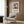 May include: Framed Henri Matisse exhibition poster featuring abstract blue figures in cut-out style with orange and yellow accents, displayed above a beige upholstered armchair with geometric pillow in modern living room with wood paneling, brass floor lamp, and side table with open book.