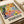May include: Colorful Matisse-style exhibition poster featuring abstract fruit and flowers in vibrant yellows, oranges, blues, and greens with text "Discover the Art of Henri Matisse" displayed on white surface next to cream-colored lamp and neutral home decor