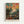 May include: Framed art print in light wood frame mounted on white wall. Colorful impressionist painting showing figures in an orchard with fruit trees under vibrant sky in blues, oranges, and yellows. Bold brushstrokes create textured landscape scene. Text "HENRI MATISSE PARIS" appears at bottom of print in black letters on cream background.