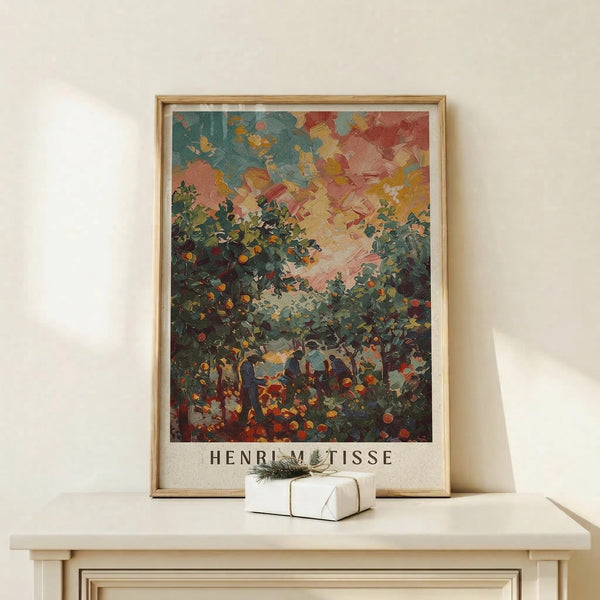 May include: Framed art print featuring an impressionistic landscape with vibrant orange and pink sky, lush green foliage with small orange fruits, and silhouetted figures beneath trees. The artwork displays thick, expressive brushstrokes in a post-impressionist style. Set in natural wood frame on light wooden surface with small white gift box and pine sprig against cream wall.