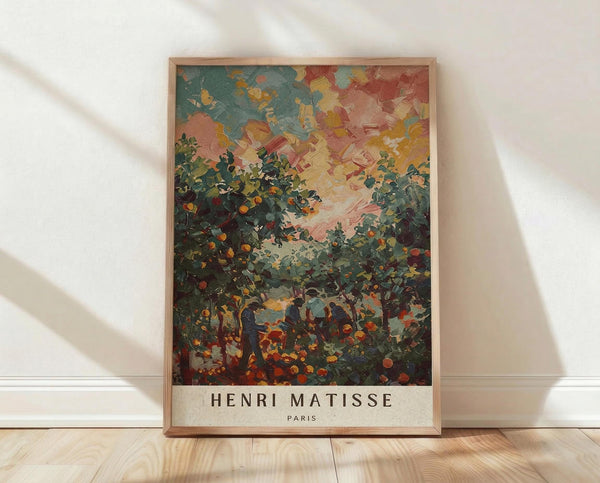 May include: Framed art print featuring an impressionistic landscape painting with vibrant brushstrokes in blues, greens, oranges, and reds depicting foliage and sky. The artwork shows thick paint texture and bold color contrasts typical of post-impressionist style. Text reading "HENRI MATISSE PARIS" appears at bottom. Light wooden frame sits on pale wood flooring against white wall with natural lighting creating soft shadows.