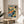 May include: Framed Henri Matisse landscape print in warm wood frame, displaying vibrant watercolor-style artwork with orange, blue, and green brushstrokes depicting Mediterranean hillside scene with trees and buildings. Print sits on round wooden side table next to beige upholstered chair in bright, naturally-lit room with white walls and plant shadows.