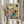 May include: Person in beige ruffled sleeves holding framed Henri Matisse landscape print featuring vibrant watercolor-style brushstrokes in blues, oranges, greens, and yellows depicting rolling hills, trees, and buildings. Dried wheat stalks visible on left side against soft neutral curtained background.