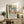 May include: Framed poster featuring a vibrant tropical landscape with palm trees, lush foliage, and warm sunset colors in Matisse's distinctive artistic style, displayed on a rustic wooden sideboard alongside a fern plant, ceramic lamp, and books in a cozy living room setting with neutral tones and natural lighting.