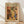 May include: Framed art print in natural wood frame leaning against white wall on light wooden floor. Poster features Henri Matisse-inspired still life with colorful vases, plants, fruits, and vessels in warm earth tones of orange, yellow, green, and blue. Bold "MATISSE" text at top. Artwork shows cut-out style botanical elements including leaves and citrus slices arranged with pottery and bowls in modernist composition.