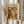 May include: Person holding framed art print featuring Henri Matisse-inspired still life with colorful vases, plants, and fruit in warm orange, yellow, green, and black tones. Light wood frame against neutral background with decorative pampas grass stems visible on left side. Hands wearing cream-colored ruffled sleeves display the vintage-style botanical artwork.