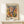 May include: Framed Matisse exhibition poster in light wood frame leaning against white wall on light wooden shelf. Features abstract cut-out style artwork with organic shapes in muted colors - peach, green, purple, yellow, and orange. Text reads "MATISSE" at top, "06200 NICE, FRANCE" and "Explore Matisse's World" at bottom. Small white wrapped gift with twine and greenery sits beside frame.