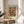 May include: Framed art print featuring abstract colorful shapes in blues, oranges, greens, and yellows with "MATISSE" text at top, displayed on light wood round side table next to beige upholstered chair and plant leaves visible in corner, soft natural lighting creating shadows on neutral wall background.