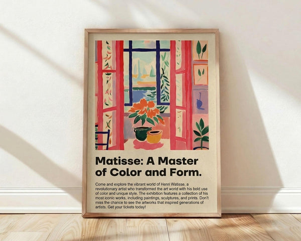 May include: Framed poster print featuring Henri Matisse-inspired artwork of an interior scene with coral red French doors opening to a window view, orange flowers in pottery, leafy plants, and vibrant fauve-style colors. Wooden frame leaning against white wall on light wood flooring with natural window shadows. Exhibition-style poster with black text describing the artist's revolutionary use of color and form.