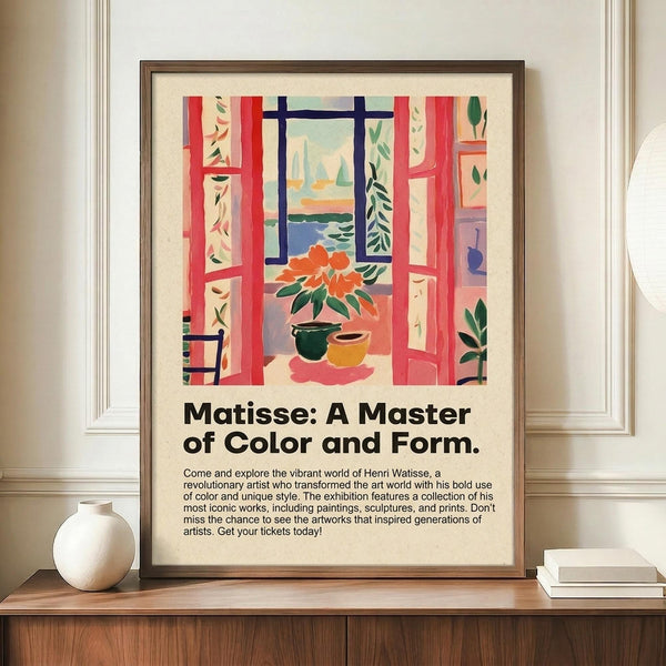 May include: A framed poster featuring a Matisse-style colorful interior scene with red window frames, potted flowers, and view of boats on water, displayed on a wooden console table next to a white ceramic vase and stacked books in a bright room with white walls and crown molding.