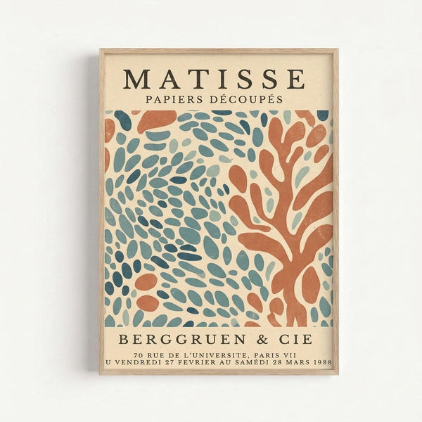 A framed exhibition poster featuring abstract organic shapes in teal blue-green and terracotta orange on a cream background. The design shows flowing, leaf-like forms scattered across the composition in Matisse's signature cut-out style. Black text at top reads "MATISSE PAPIERS DÉCOUPÉS" and bottom text shows gallery and exhibition details. The poster is displayed in a light wood frame against a white wall.