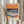 May include: Person in beige clothing holding framed art print featuring abstract seascape with orange sunset sky, teal rolling waves, and sandy beach in layered collage style. Natural wood frame against white curtained window with dried pampas grass decoration visible to left.