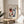 May include: Framed Henri Matisse-style portrait print displayed on light wood round side table. The artwork features an abstract face with asymmetrical coloring - orange-red around one eye, blue shadowing on the other side, red lips, and black eyebrows against cream background. Natural lighting creates soft shadows on beige wall behind. Green plant leaves visible in corner, neutral fabric chair arm on right.