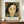 May include: Framed art print featuring a portrait of a woman with black wavy hair and pale skin against a colorful floral background in warm orange, green and blue tones. The poster shows Henri Matisse's name and a quote about flowers at the bottom. The frame sits on a wooden sideboard next to a white ceramic vase and books in a bright room with white paneled walls.